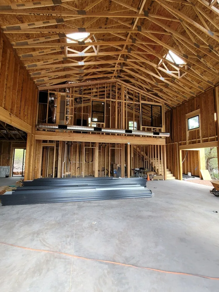 Tall interior roof framing and loft structure with construction materials on the slab