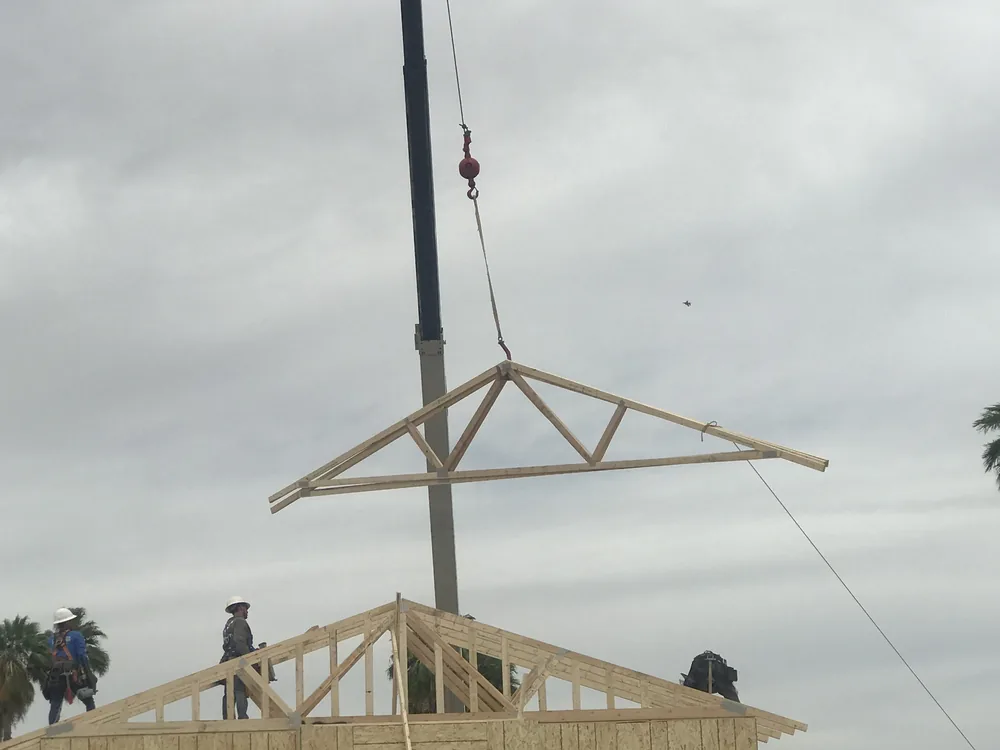 A crane lifting a wood roof truss above wall framing